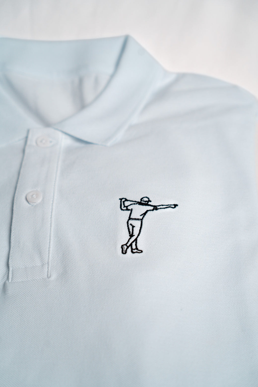 FOA white polo, close-up of the embroidered golfer and fabric.