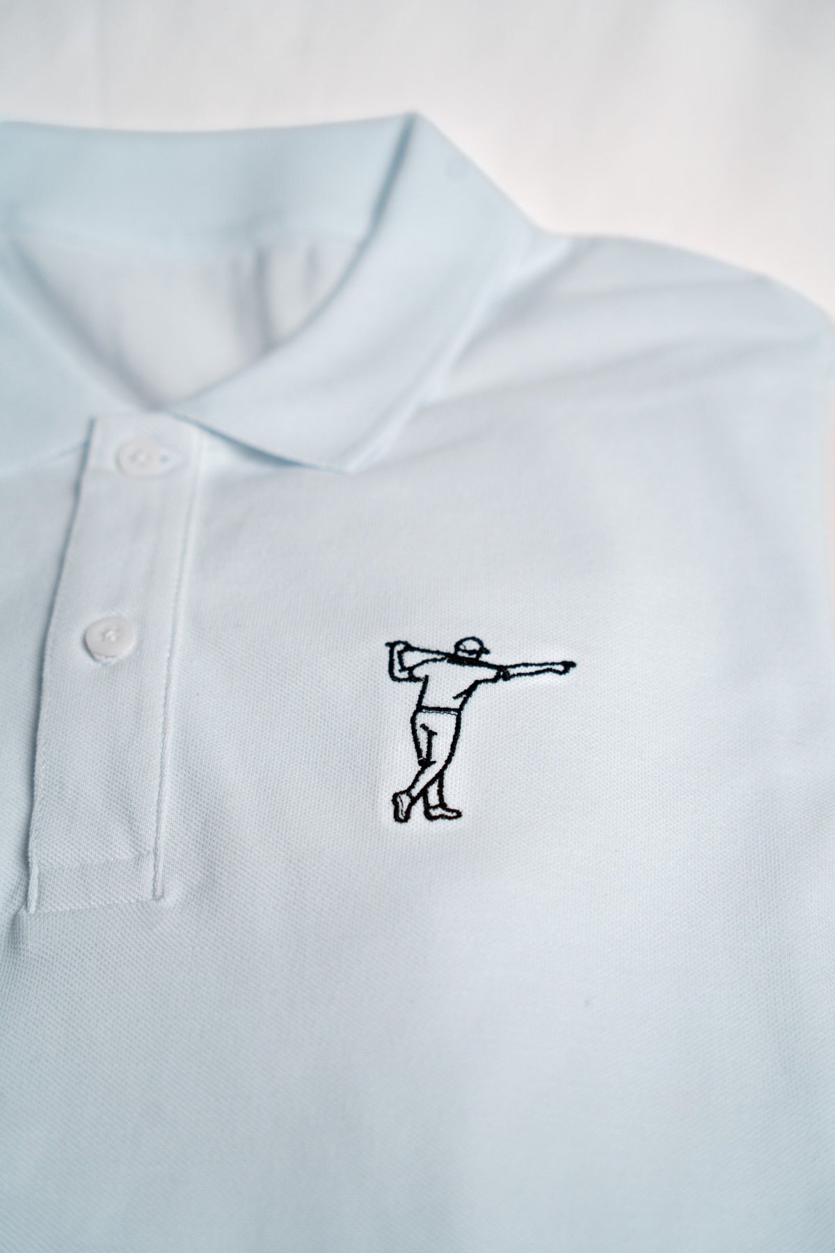 FOA white polo, close-up of the embroidered golfer and fabric.