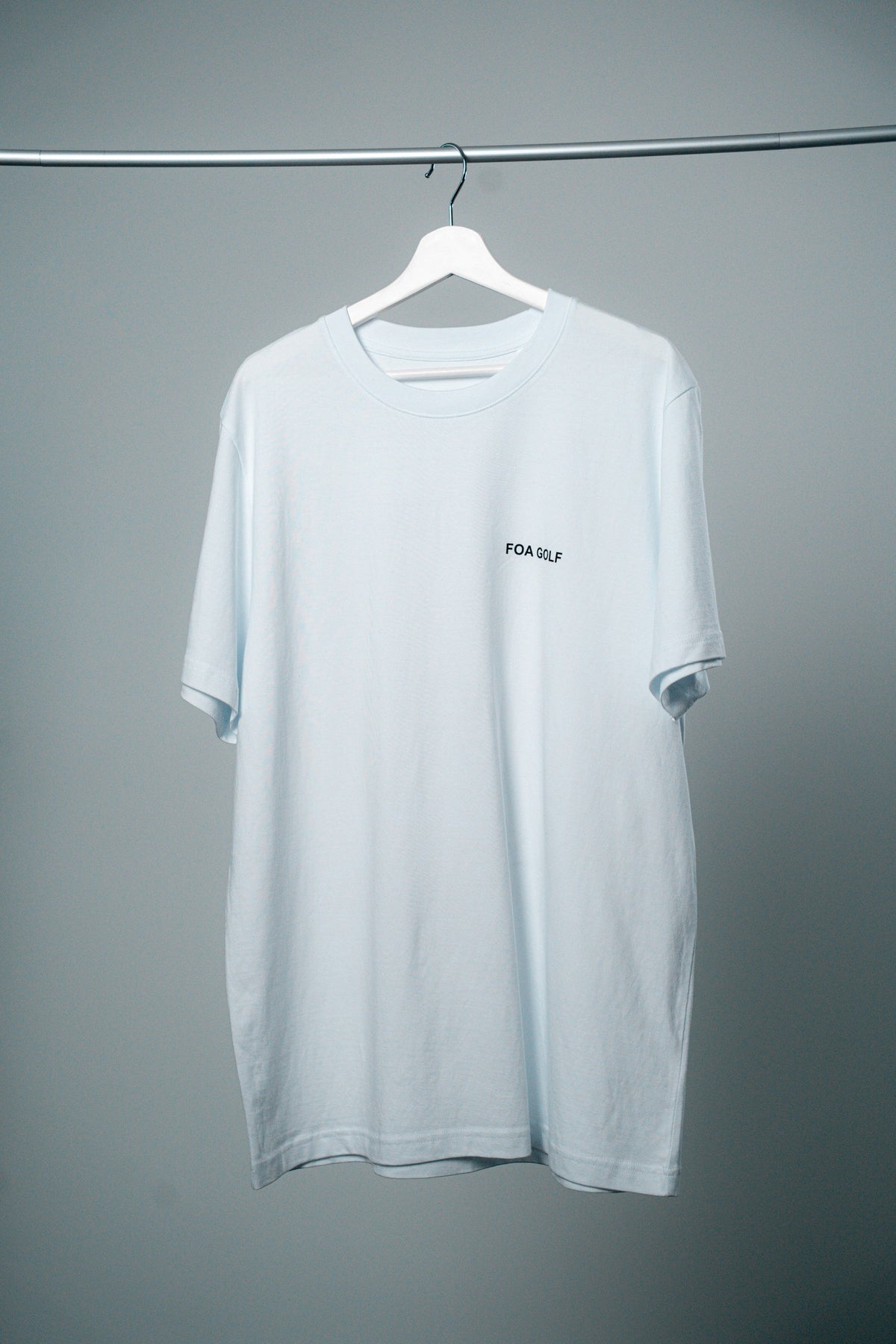 FOA t-shirt, vit, framifrån på en galge.